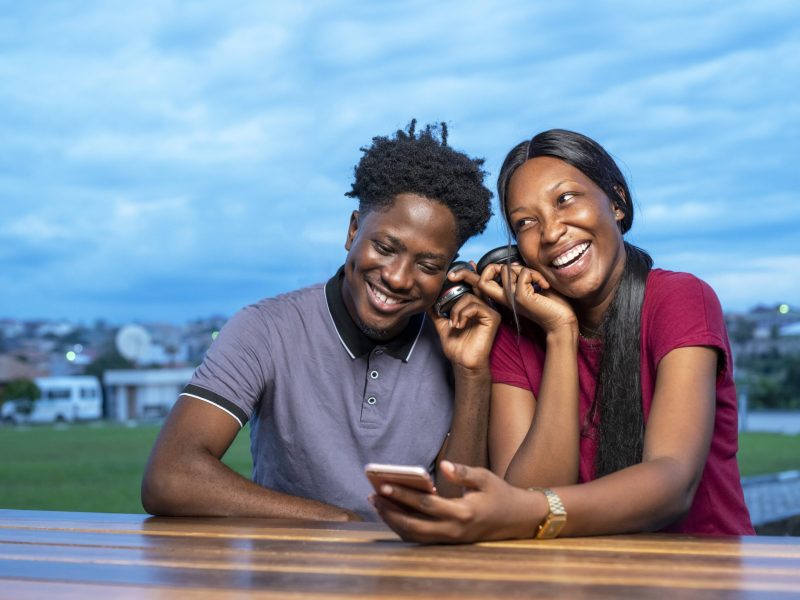 A cute African couple sitting in a park and watching a funny video together